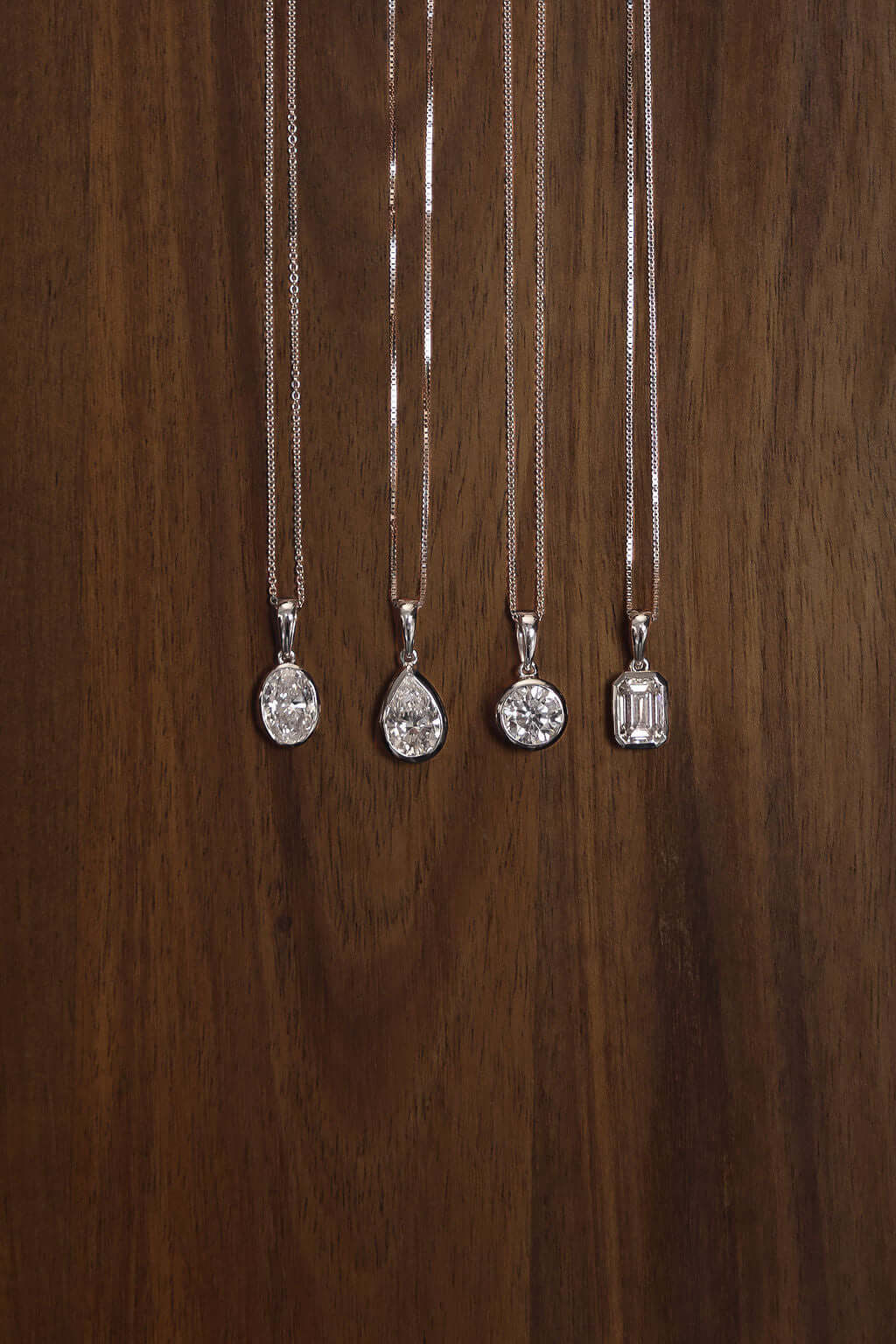 Four elegant pendants including a 1ct Oval Lab Diamond Bezel Pendant displayed on wooden background.