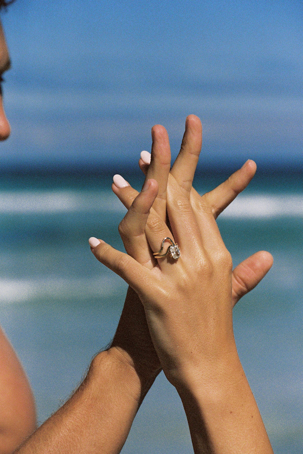 Two hands with a ring held up against a blurred beach background