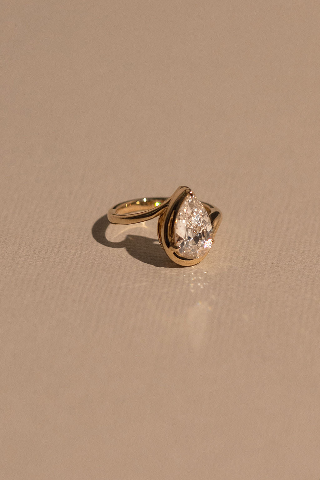 Gold ring with a pear-shaped diamond on a beige background