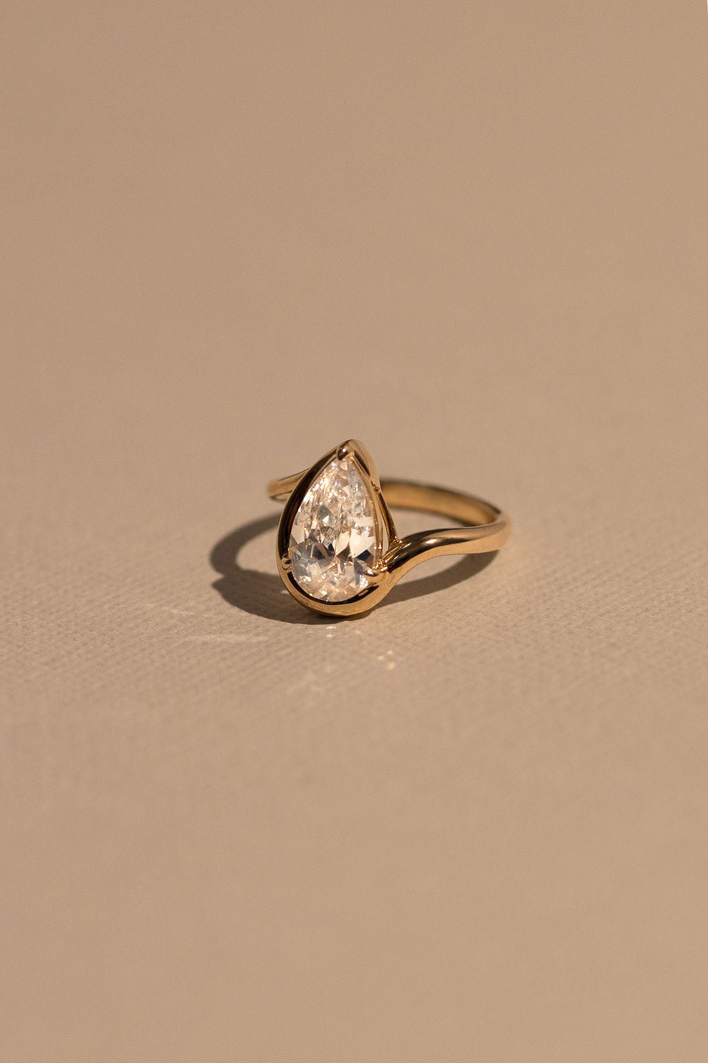 Gold ring with a teardrop-shaped diamond on a beige background