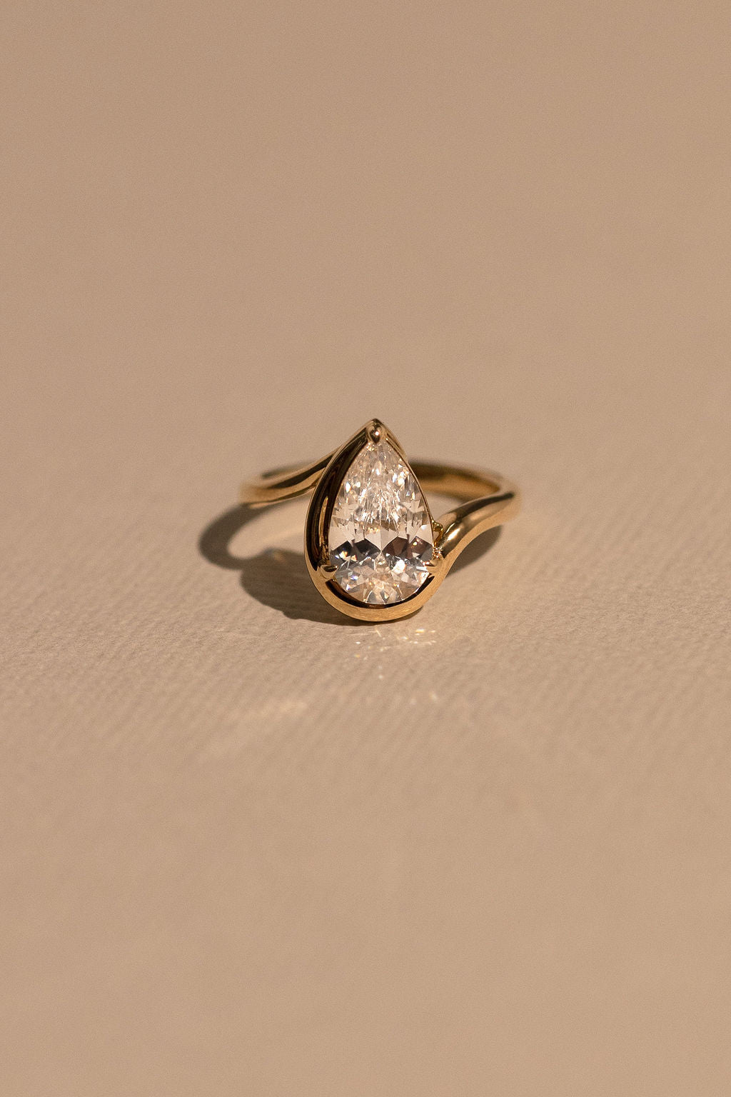 Gold ring with a teardrop-shaped diamond on a beige background