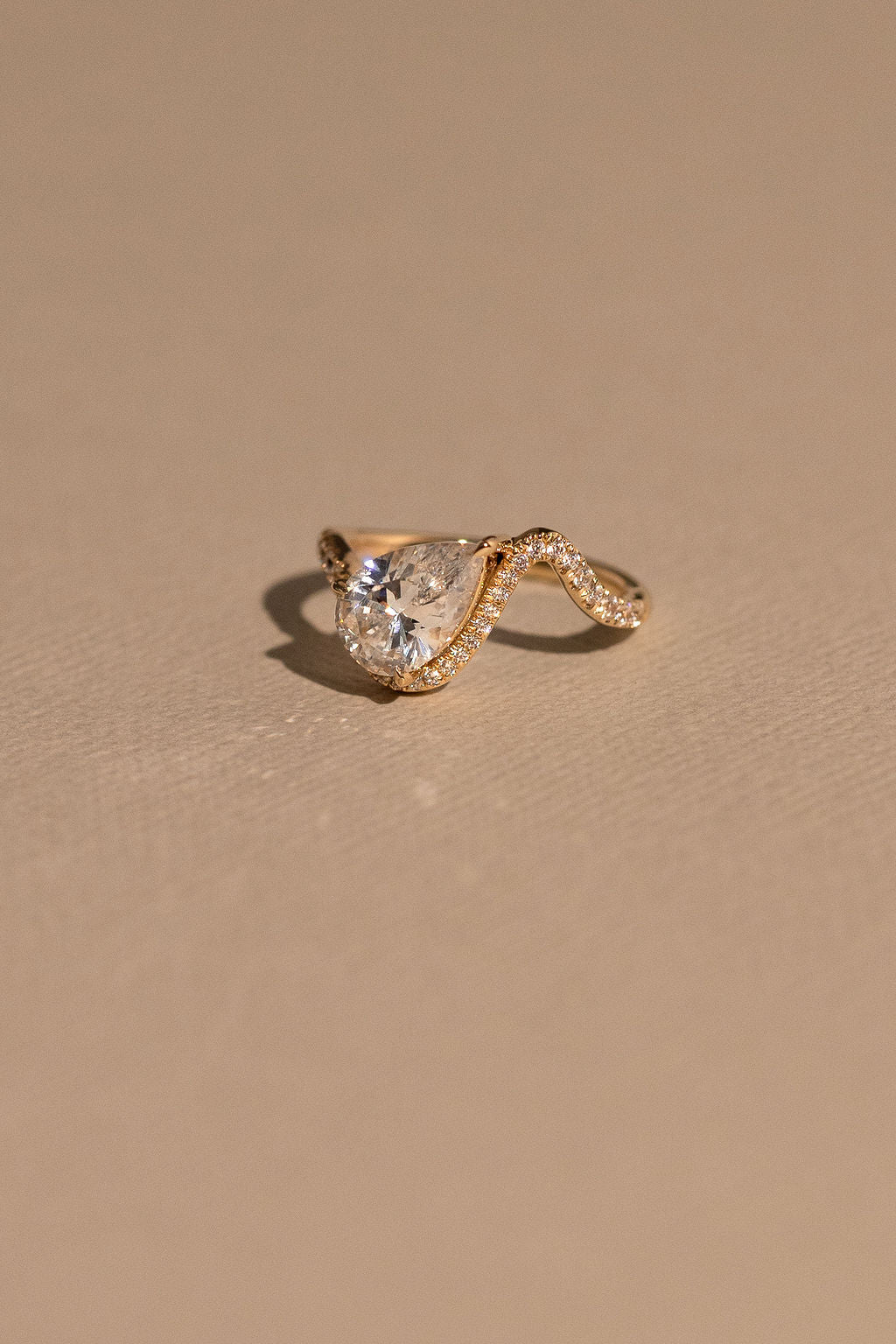 Gold ring with a teardrop-shaped diamond on a beige background