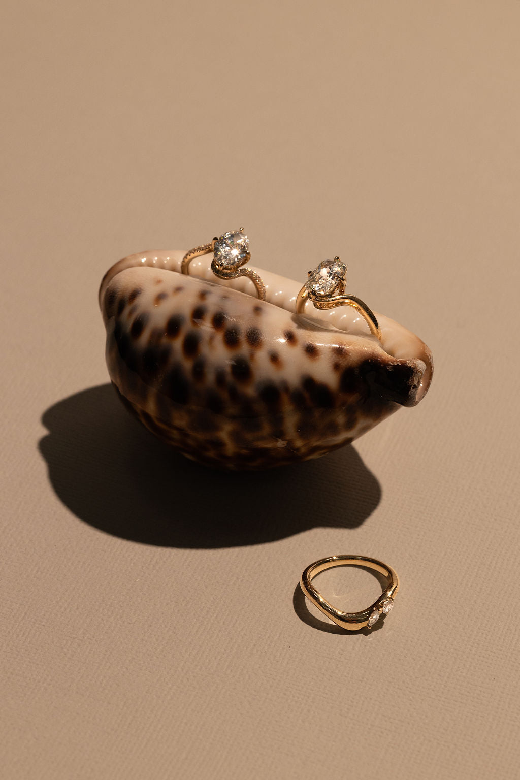 Gold rings with diamonds on a shell against a beige background