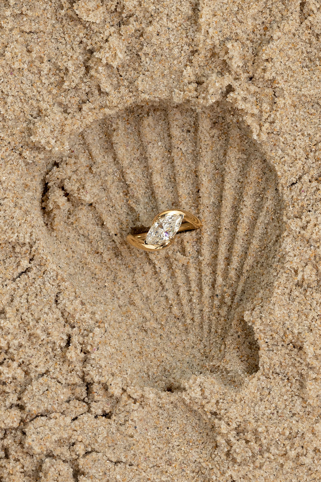 Gold ring with a diamond on a sand imprint of a shell