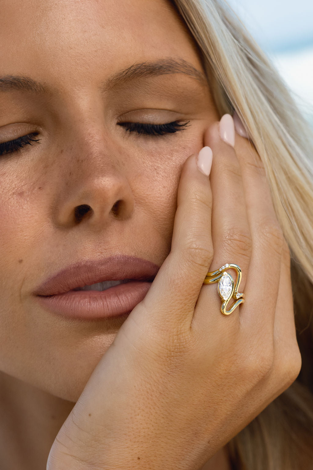 Close-up of a woman wearing a gold ring with a diamond, touching her face.