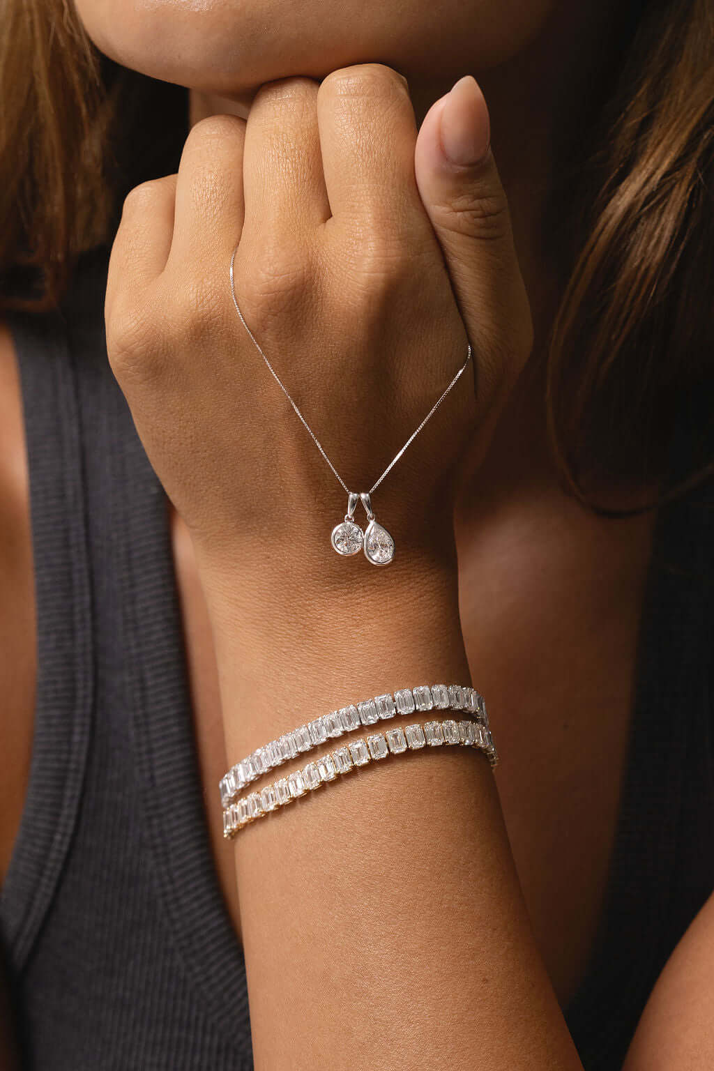 Close-up of a hand wearing a 1ct Pear Lab Diamond Bezel Pendant and elegant bracelets.