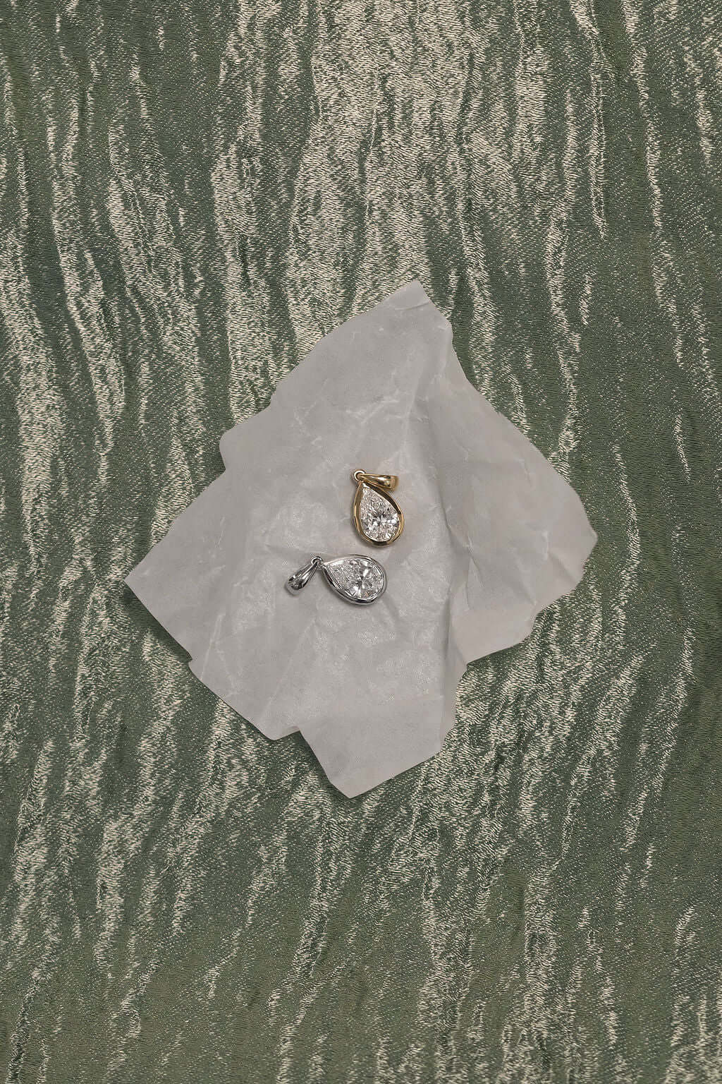 1ct Pear Lab Diamond Bezel Pendant on crumpled paper against textured green background.