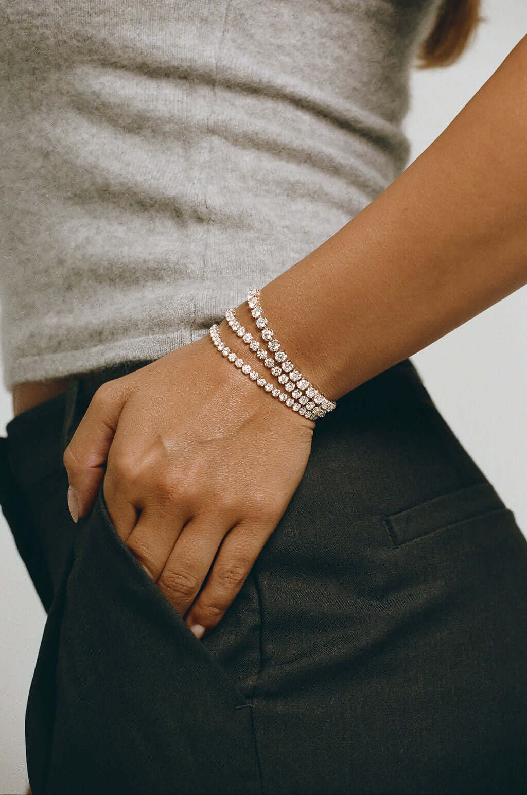 Elevated Round Tennis Bracelet 4.9ct Lab Diamond worn on a woman's wrist with dark pants and a grey top.
